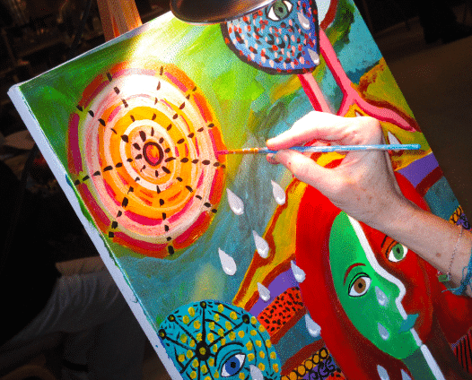 closeup of a hand holding a paint brush and painting a colorful composition onto canvas