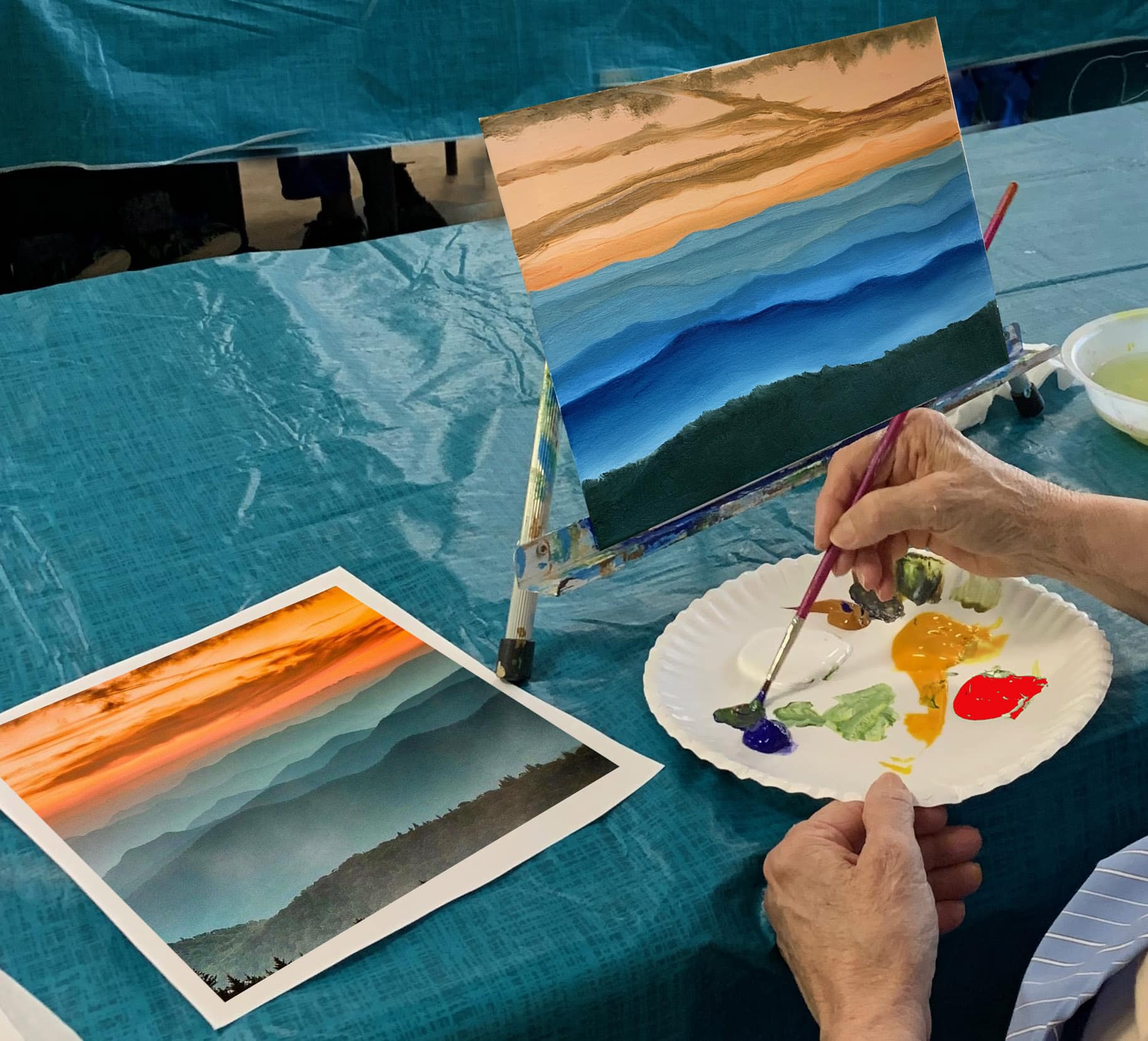 person painting a mountain landscape, holding a paint palette