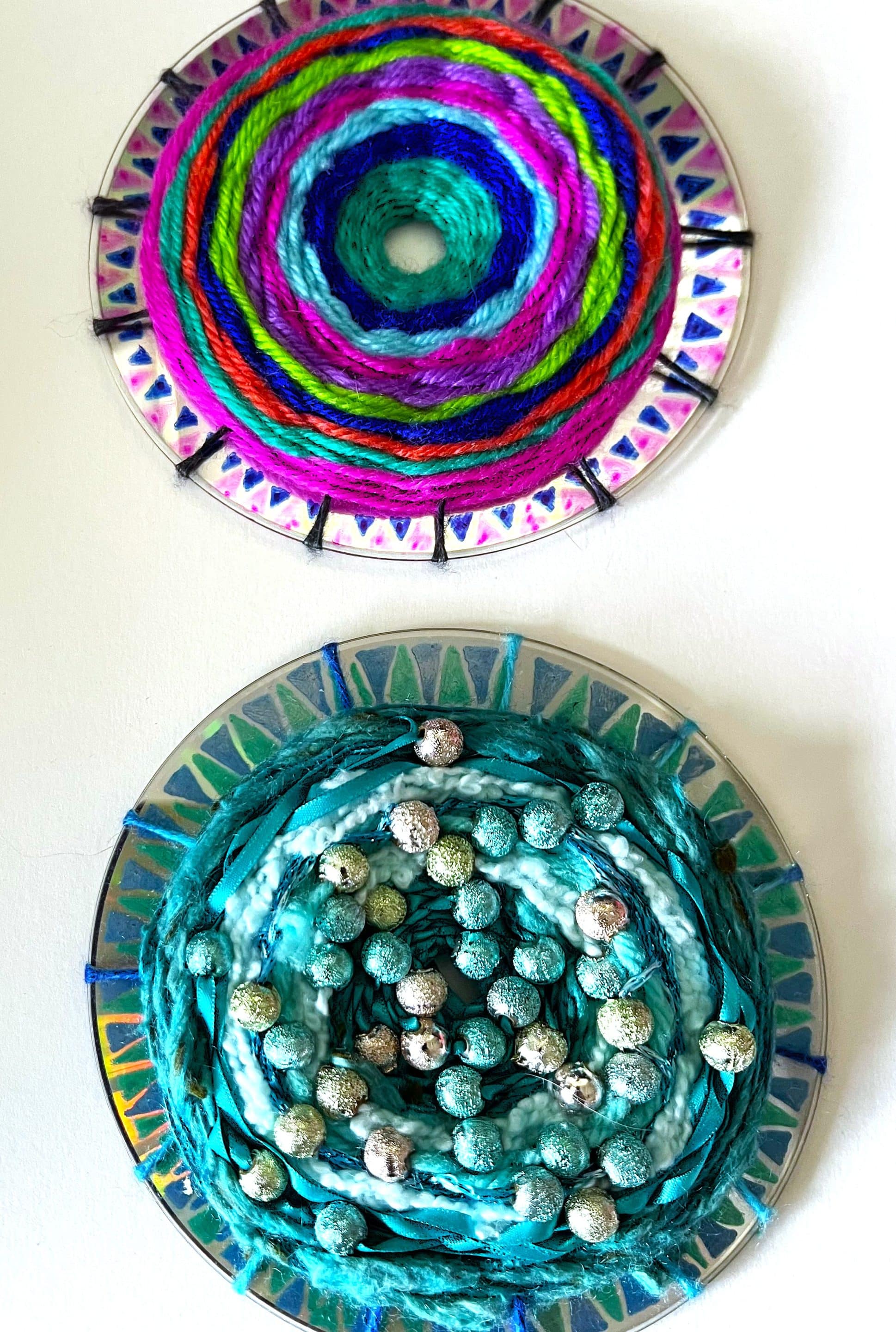 two CDs decorated with colorful yarn, woven with beads